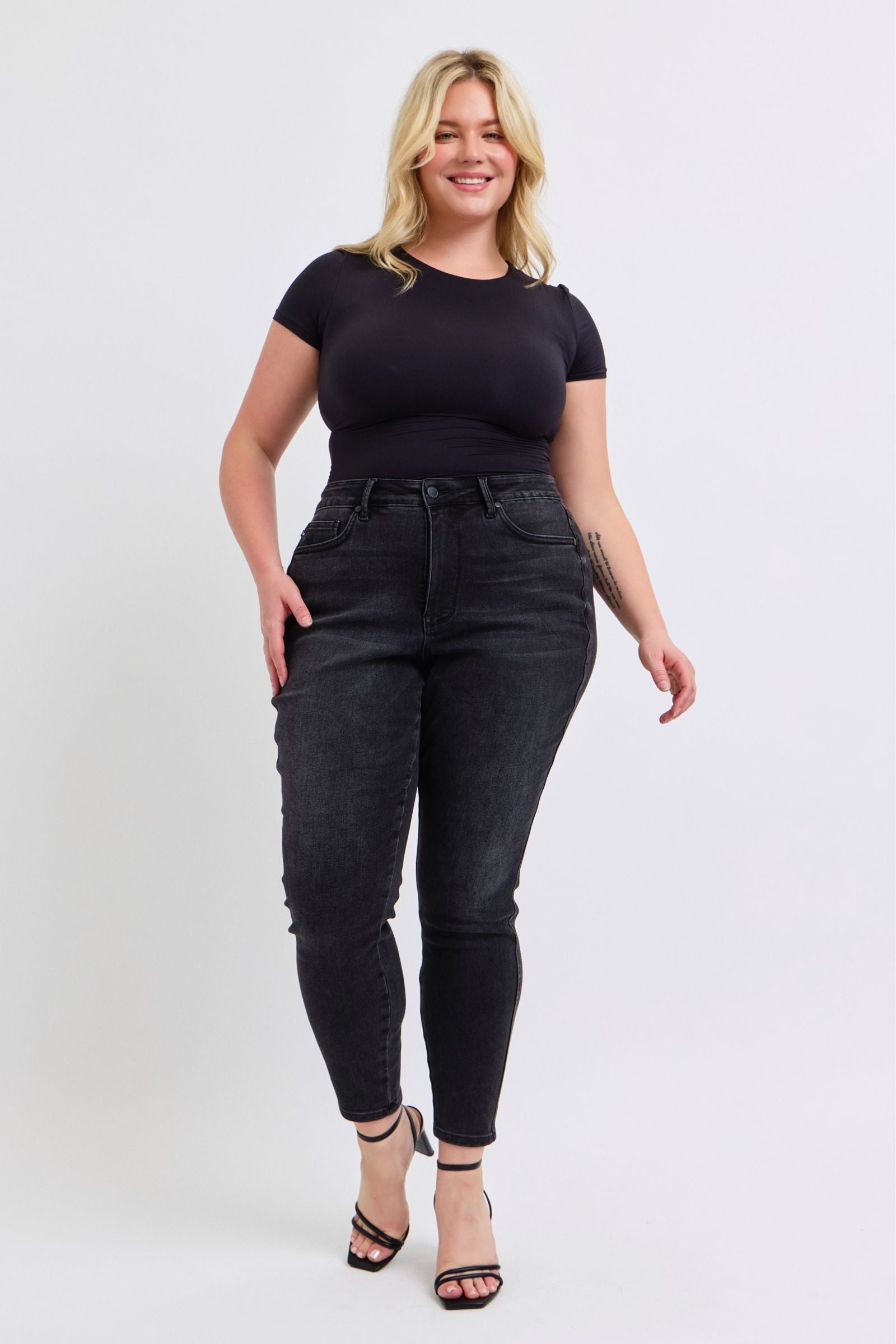 Woman wearing mid-rise faded black Judy Blue Jeans with tummy control and skinny fit paired with black top and heels