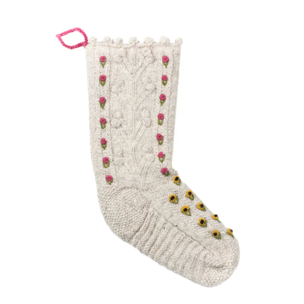 Hand-knitted Nordic Charm Christmas Stocking in natural wool with cable patterns, embroidered pink and yellow floral details, scalloped edge, and pink hanging loop.