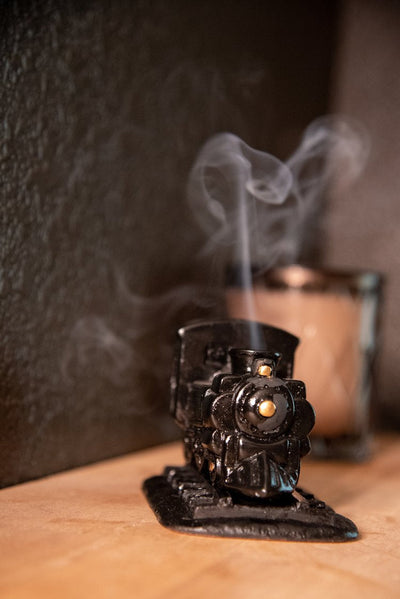 Vintage-style steam engine incense burner with smoke releasing from chimney, creating calming aromatic ambiance