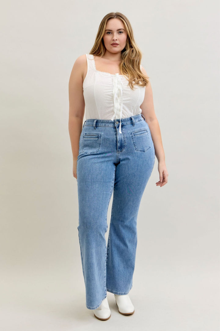 Plus size model wearing high-rise flare Judy Blue Jeans 881055 in soft stretch denim with front patch and welt pockets, styled with white top and boots.