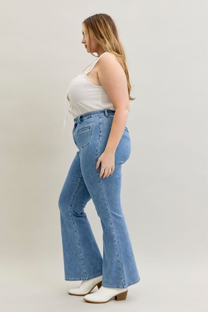 Plus size model wearing high-rise flare Judy Blue Jeans in soft stretch denim with front patch and welt pockets, styled with white top and boots