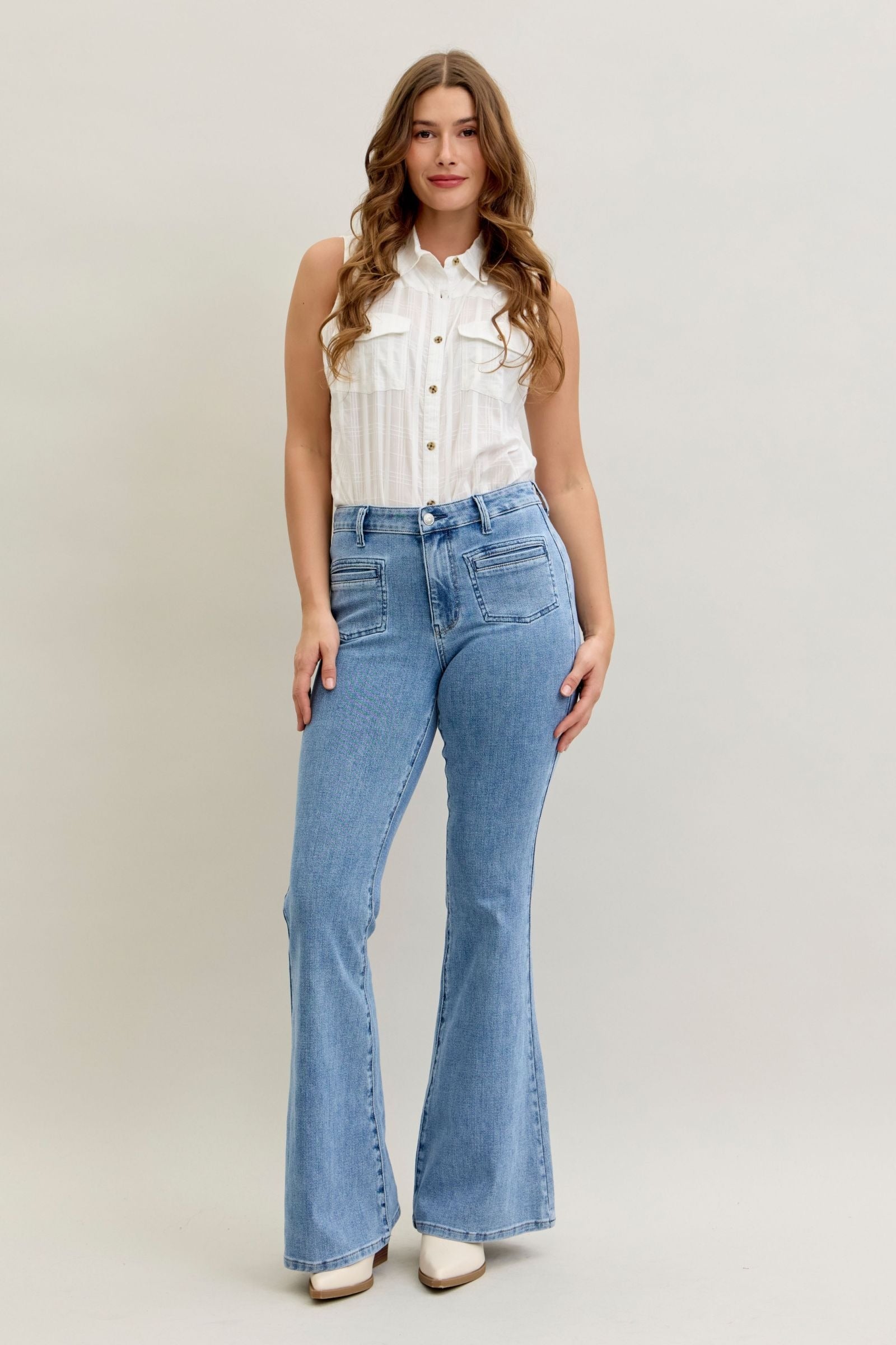 Plus size model wearing high-rise flare Judy Blue Jeans 881055 in soft stretch denim with front patch and welt pockets, styled with white top and boots.