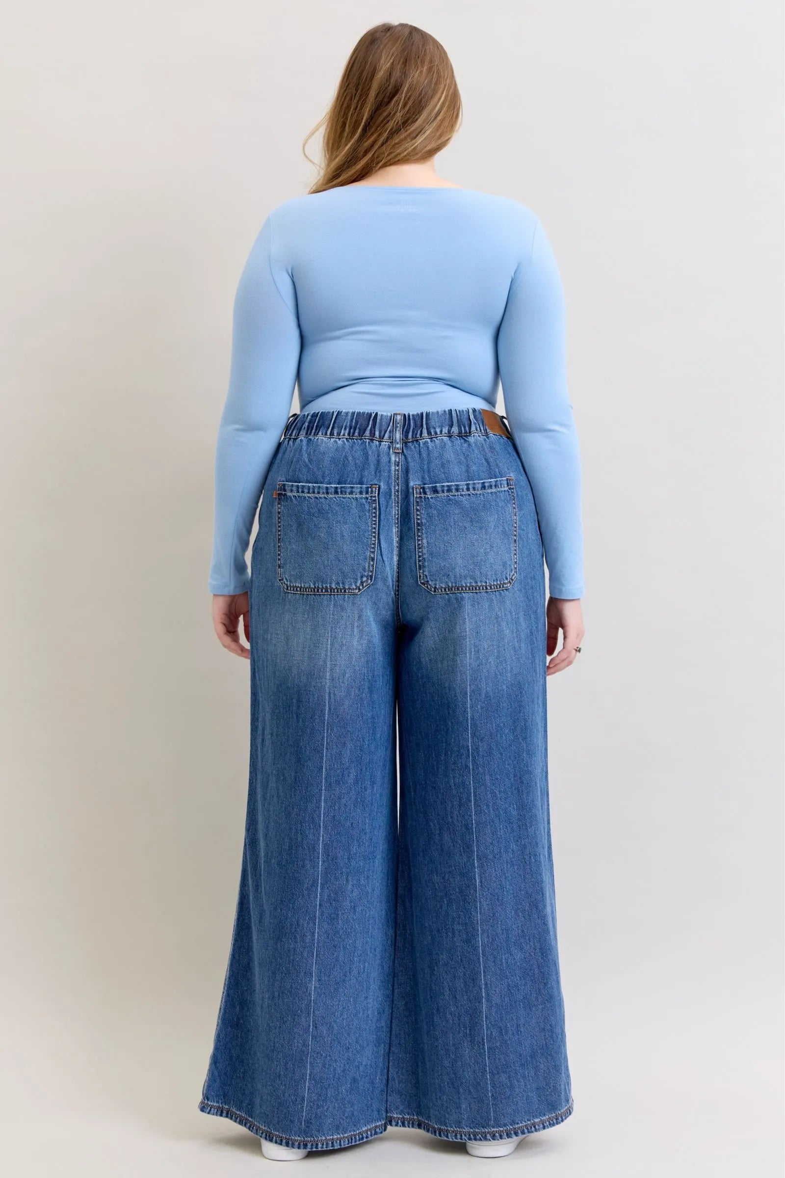 Back view of a woman wearing high waist featherweight palazzo jeans by Judy Blue Jeans with elastic waistband and wide-leg cut