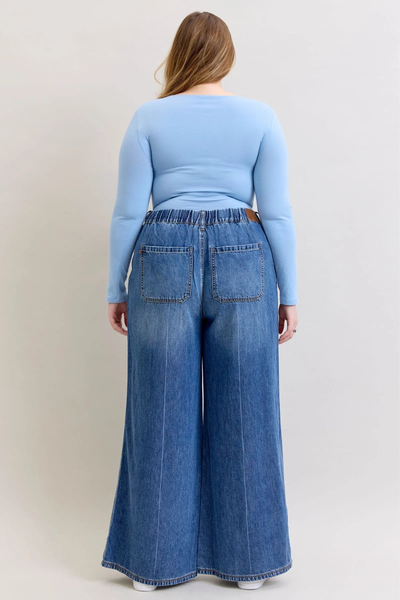 Back view of a woman wearing high waist featherweight palazzo jeans by Judy Blue Jeans with elastic waistband and wide-leg cut