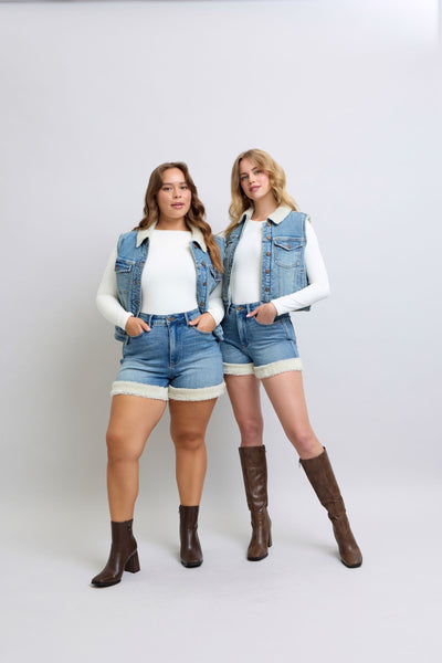 Two women wearing Judy Blue high-waisted tummy control shearling cuff denim shorts with denim vests and boots