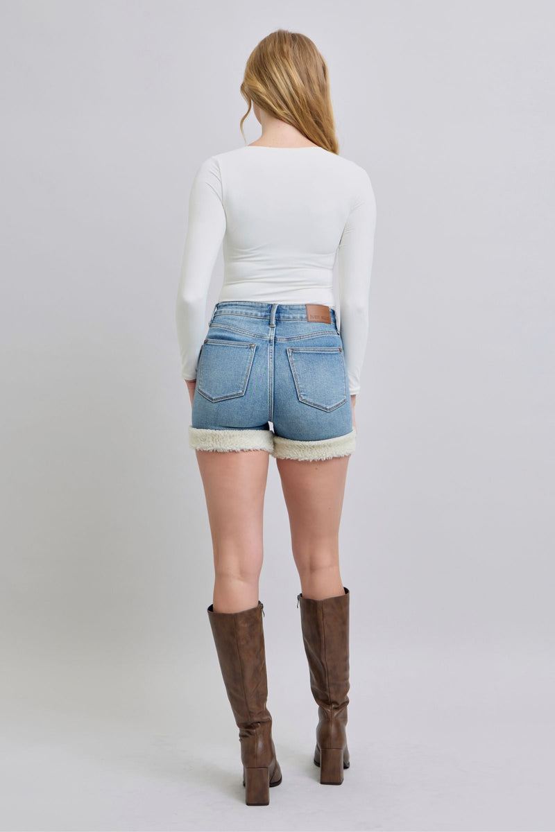 Rear view of woman wearing high-waisted Judy Blue denim shorts with shearling cuffs and brown boots