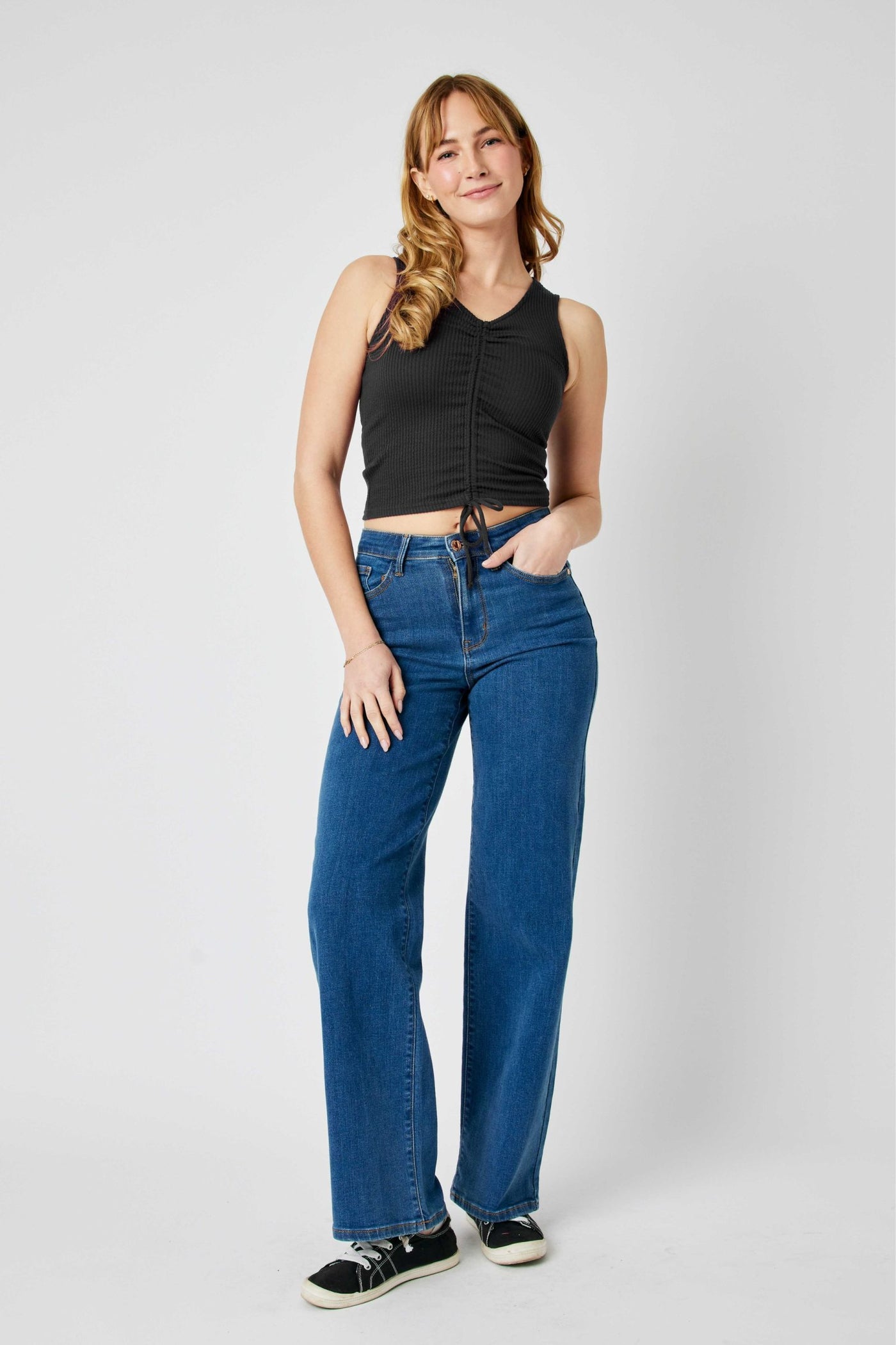 Woman wearing high waisted vintage wide leg Judy Blue Jeans in blue denim with black sleeveless top and sneakers