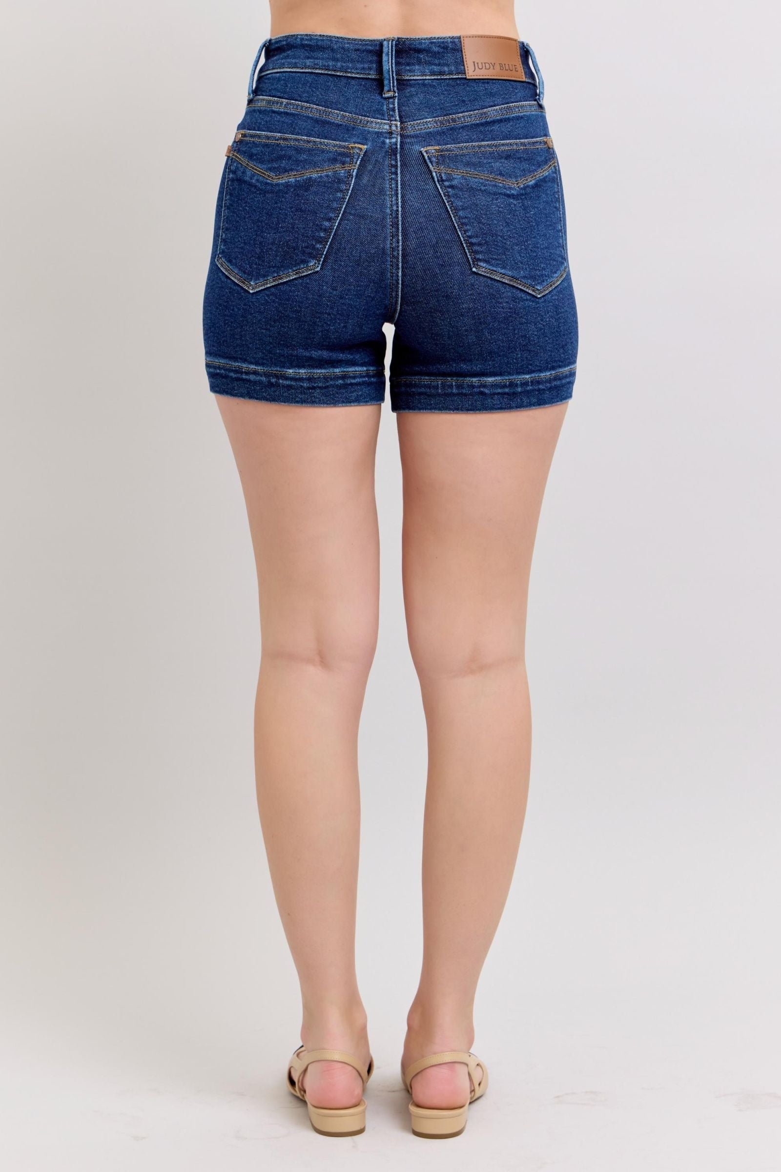 Back view of woman wearing high waist Judy Blue Shorts in dark blue denim with pockets and rolled hems