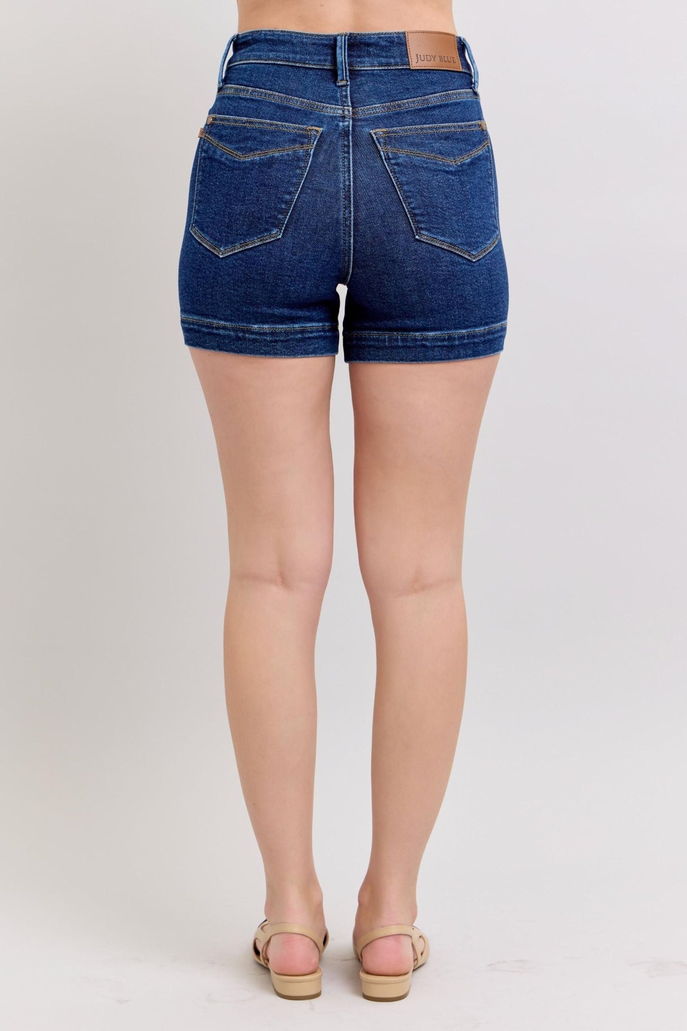 Back view of woman wearing high waist Judy Blue Shorts in dark blue denim with pockets and rolled hems