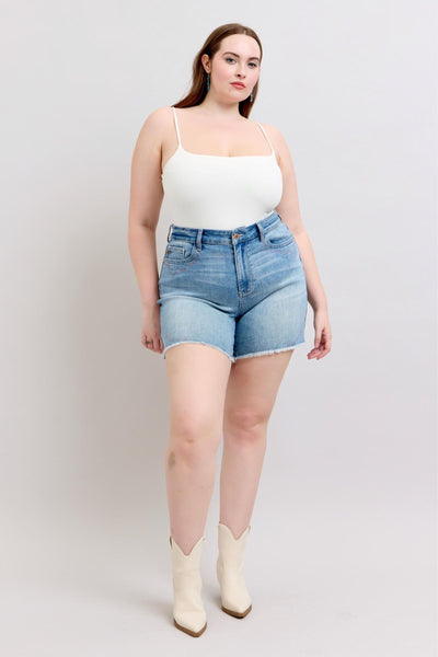 Plus-size model wearing high-rise Judy Blue Shorts with raw cut-off hem and western-style embroidery, styled with a white tank and boots.