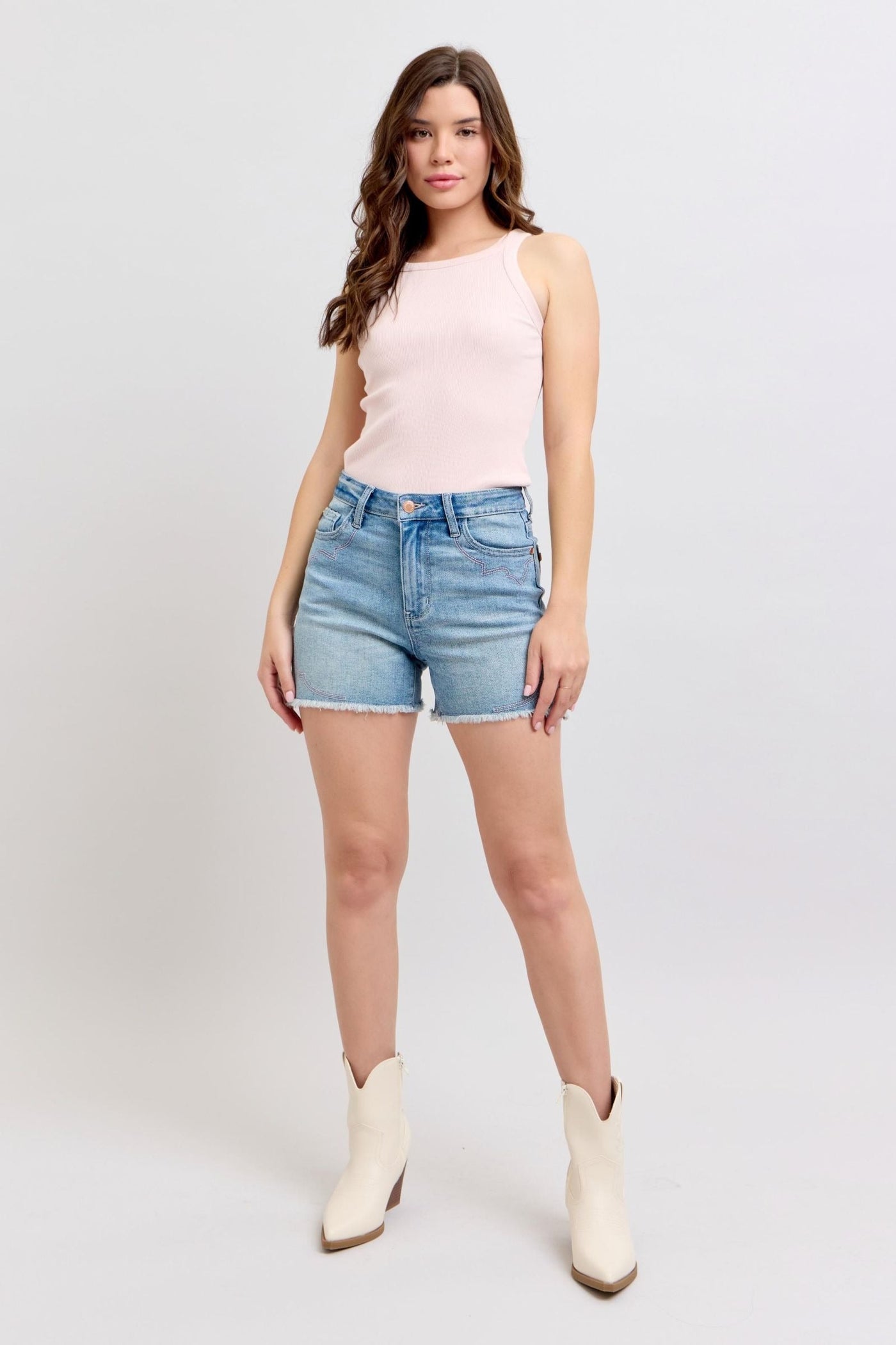 Judy Blue Shorts with high-rise cut and raw hem in light denim, modeled with white boots.