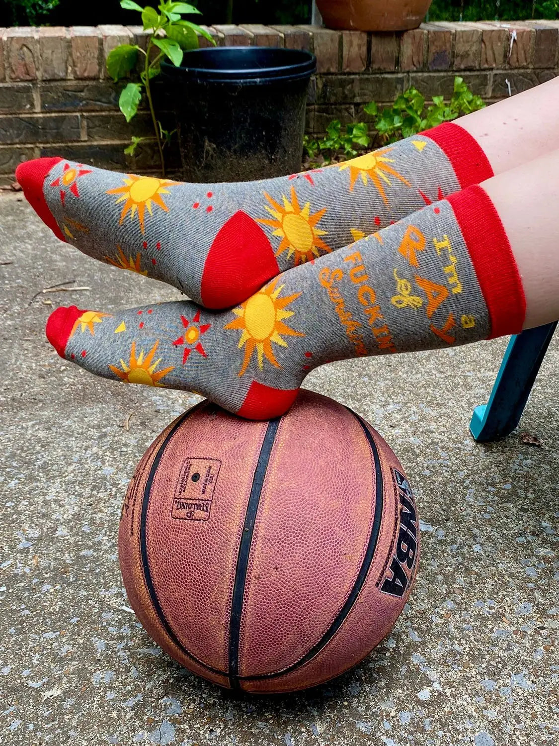 Grey women's crew socks with yellow sun designs, red accents, and "I'm a Ray of F***in' Sunshine" text, styled on a basketball outdoors.