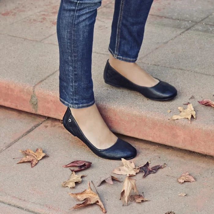 Minnetonka ANNA black leather ballerina flats worn with jeans on pavement with dry leaves