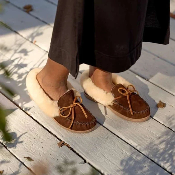 Minnetonka Alpine Sheepskin Mocs with suede and sheepskin lining, worn outdoors.