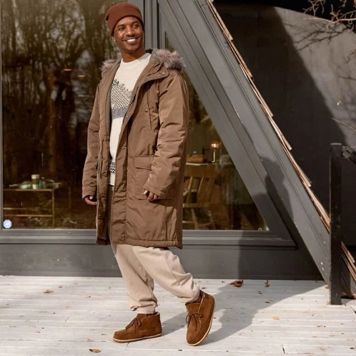 Man wearing Minnetonka Men's Torrey Shoes with brown coat and beige pants outdoors.