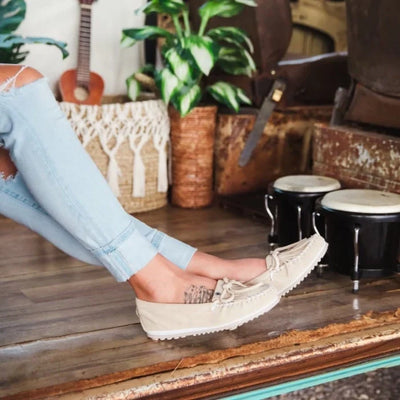 Minnetonka KILTY PLUS moccasins in beige suede, worn by a person with ripped jeans, showcasing casual style and comfort.