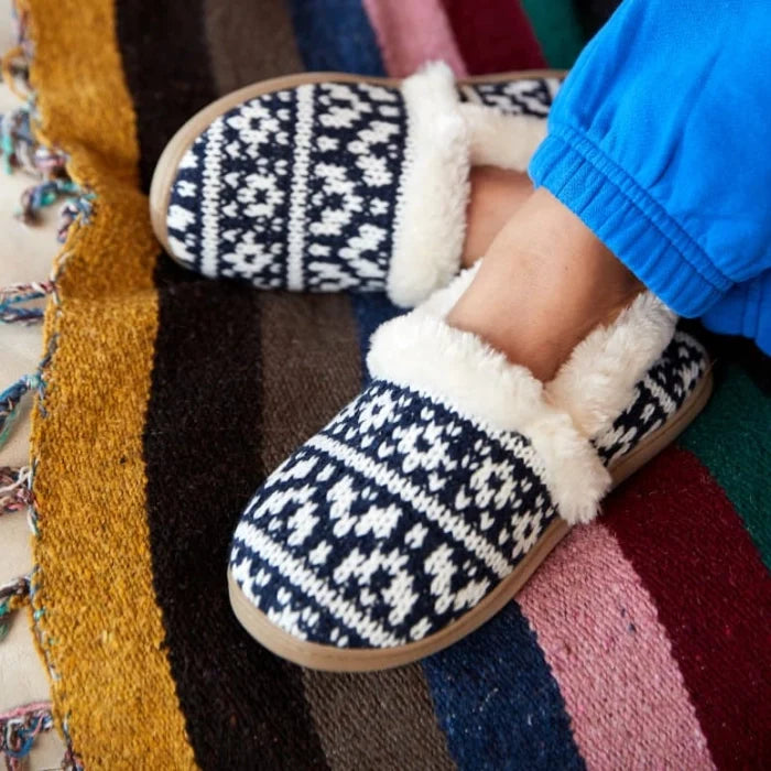 Knit-patterned Minnetonka DINA slippers with pile lining on colorful rug.