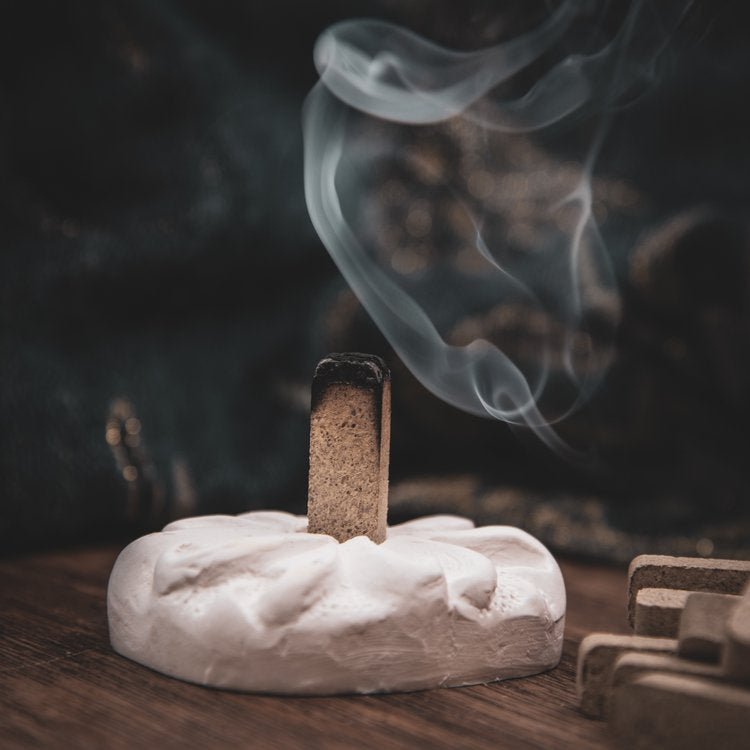 Natural wood incense brick emitting aromatic smoke in a white holder on wooden surface