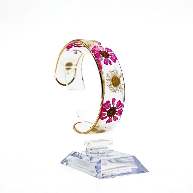 Dried flower resin cuff bracelet with pink and white flowers encased in clear resin on a display stand