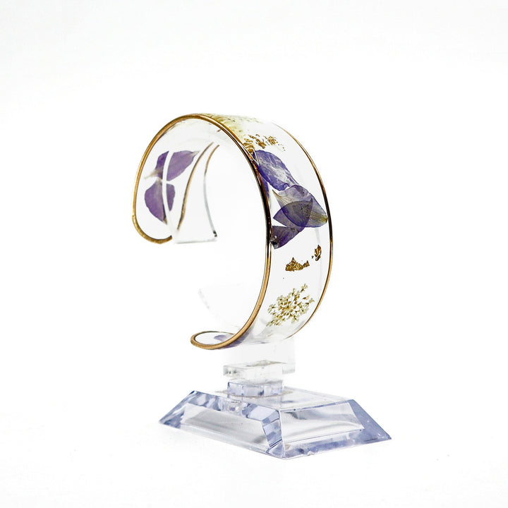 Dried flower resin cuff bracelet with real purple and white flowers encased in clear resin on a gold-edged band