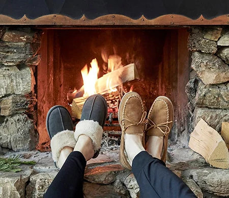 Chesney Cozy Suede Slippers with plush lining by a fireplace.