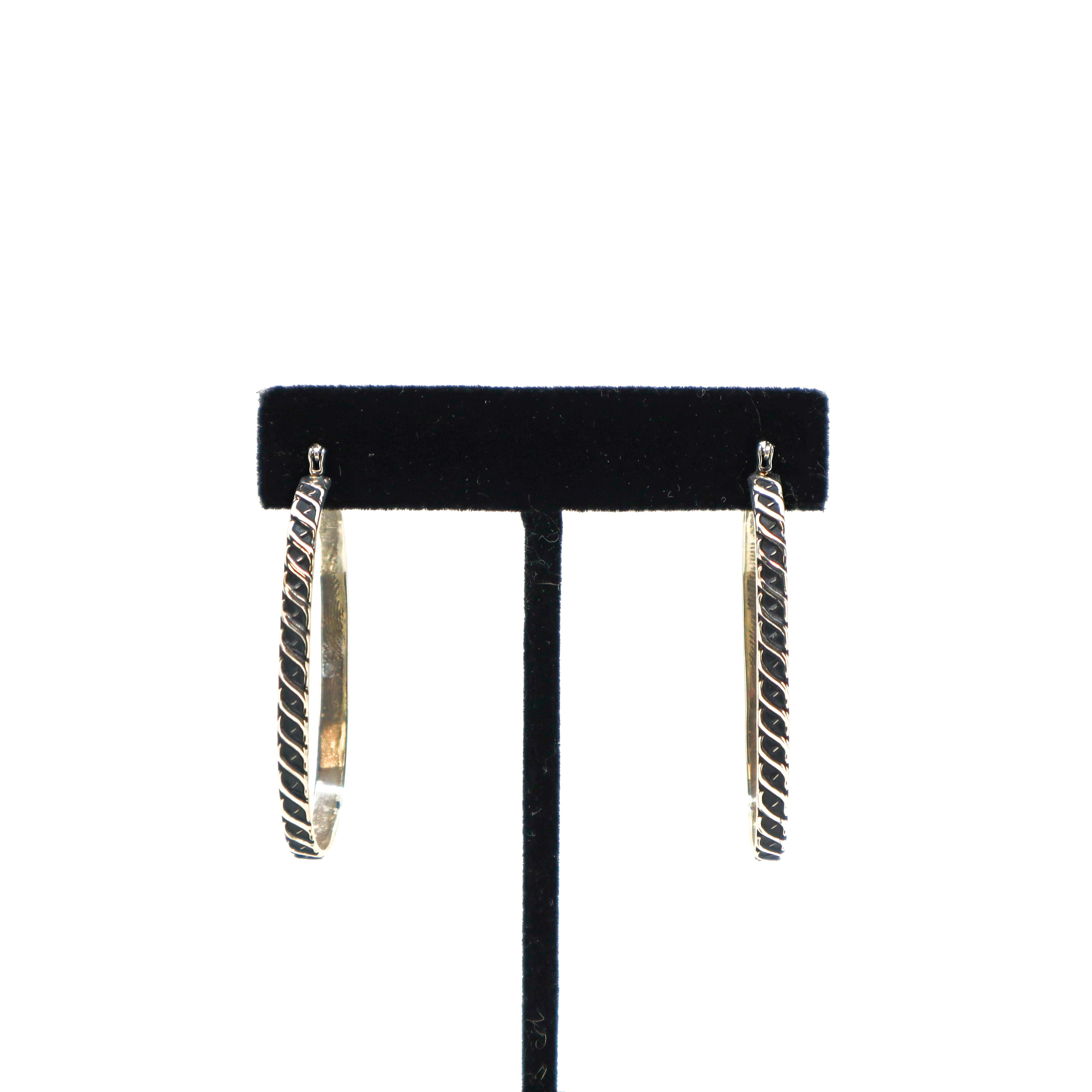 Handmade sterling silver oval hoop earrings with textured design on black stand