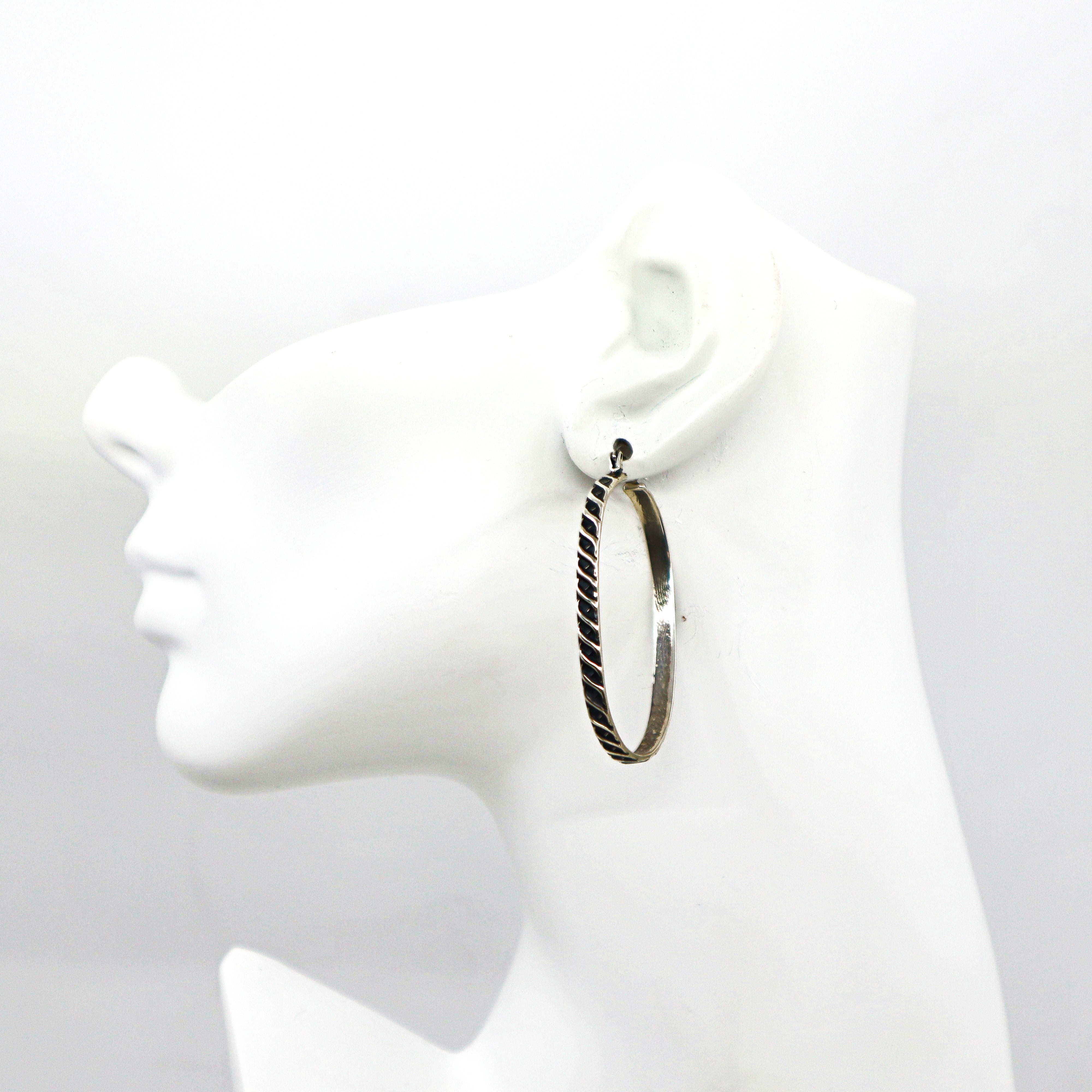 Handmade sterling silver oval hoop earrings with textured design on black stand