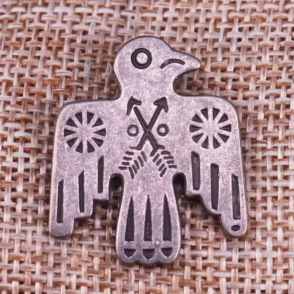 Vintage styled Thunderbird pin with crossed arrows motif on a burlap background.