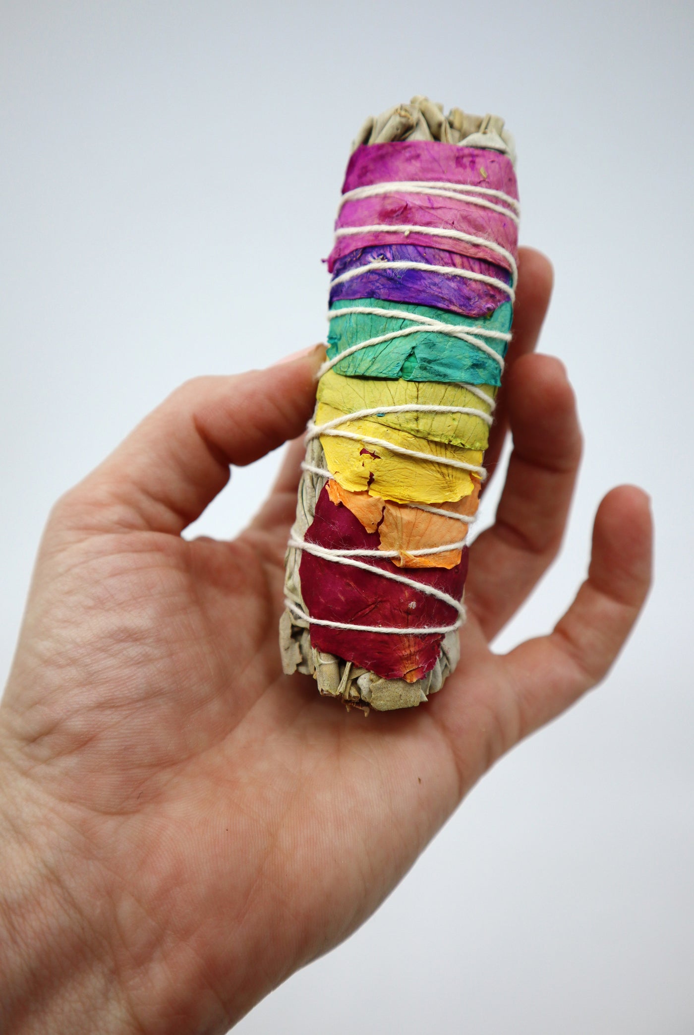 4" Sage Smudge Stick held in hand, ethically sourced and hand-harvested, featuring colorful wrappings.