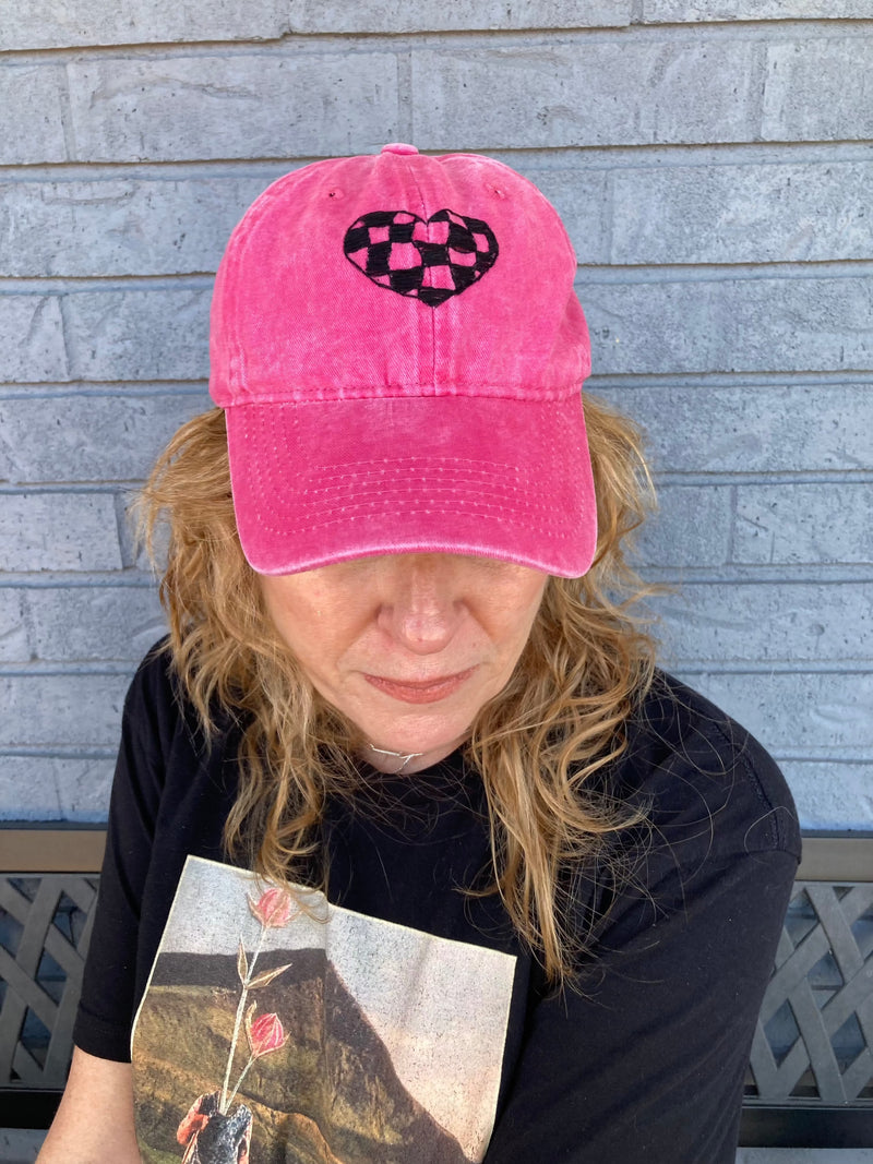 Hot pink Wild Sour Checkered Heart Hat with black checkered heart design worn by woman