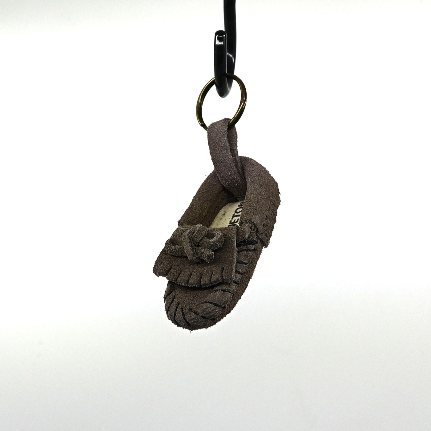 Minnetonka key ring shaped like a small brown suede moccasin hanging on a black hook