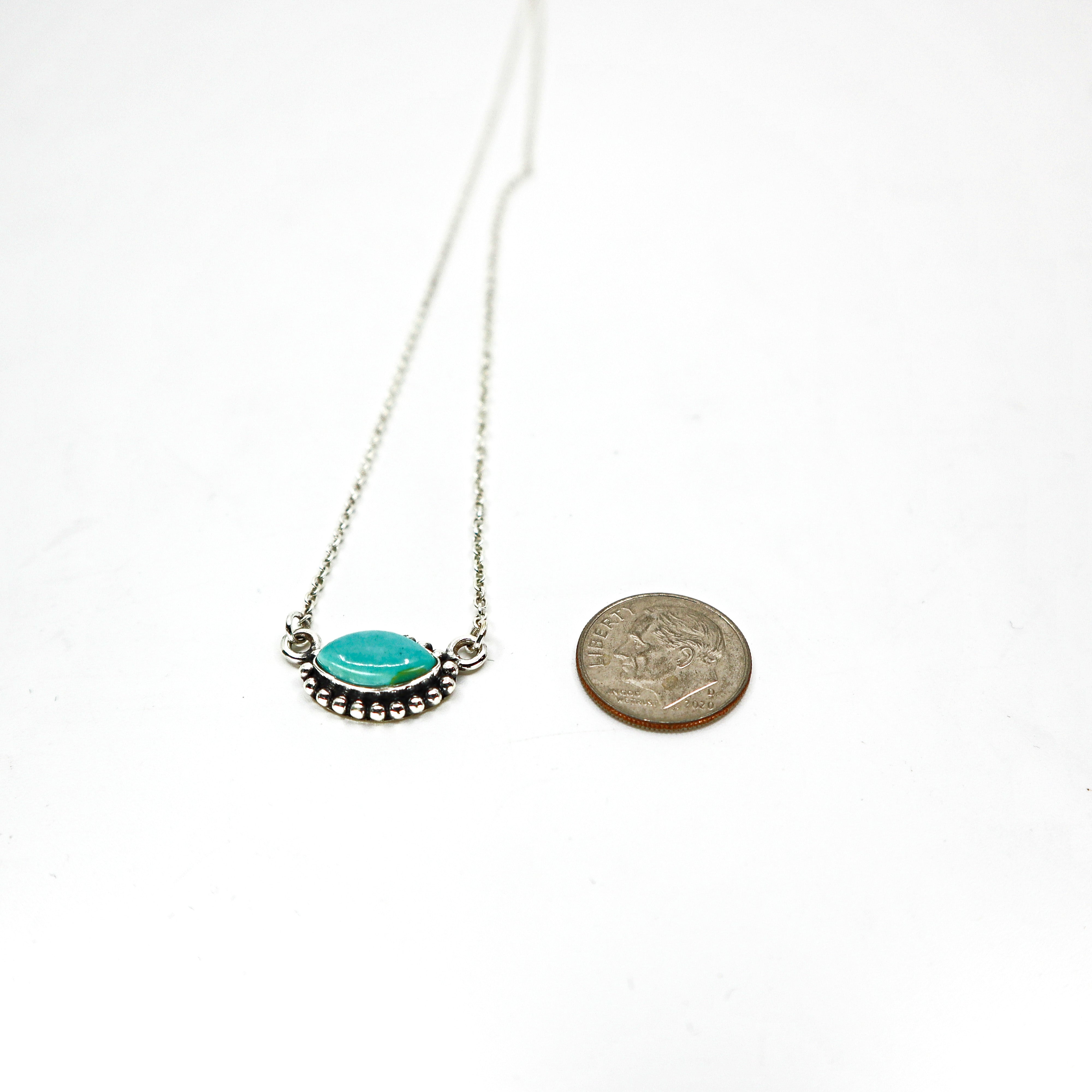 Handmade sterling silver necklace with turquoise oval pendant next to a coin for size comparison