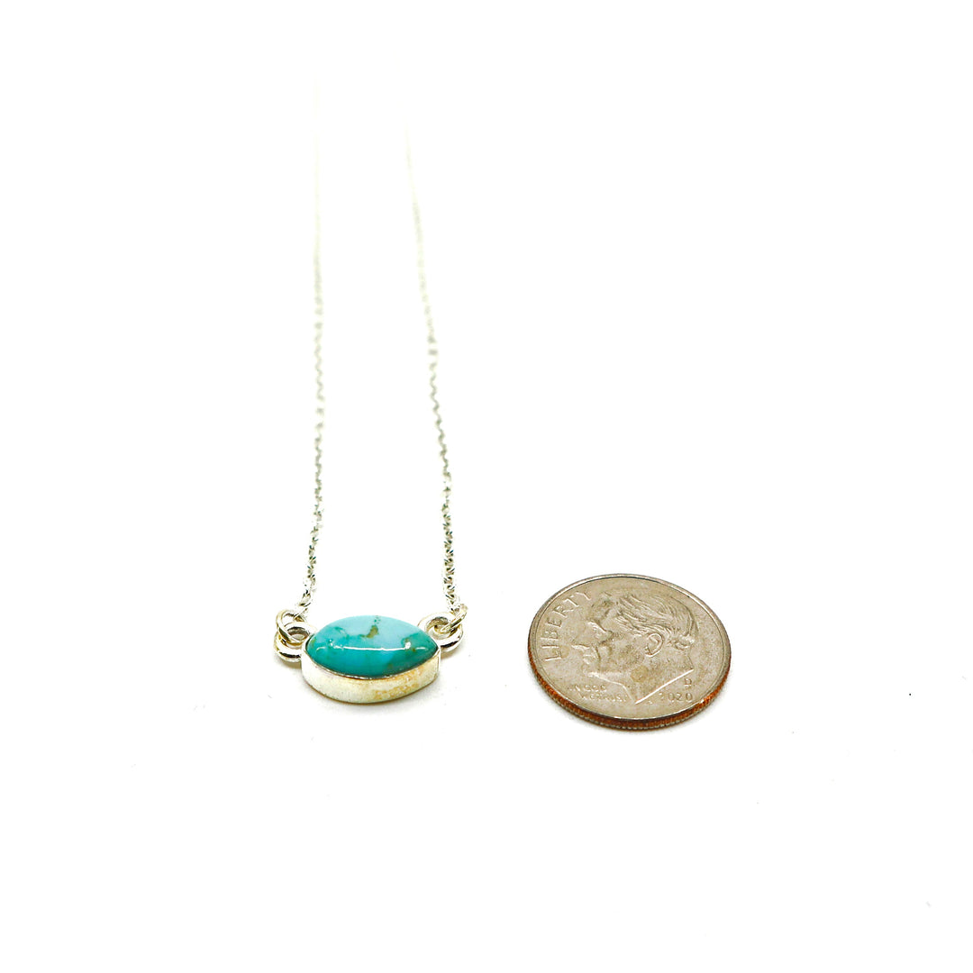 Handmade sterling silver necklace with oval turquoise pendant next to a dime for size comparison