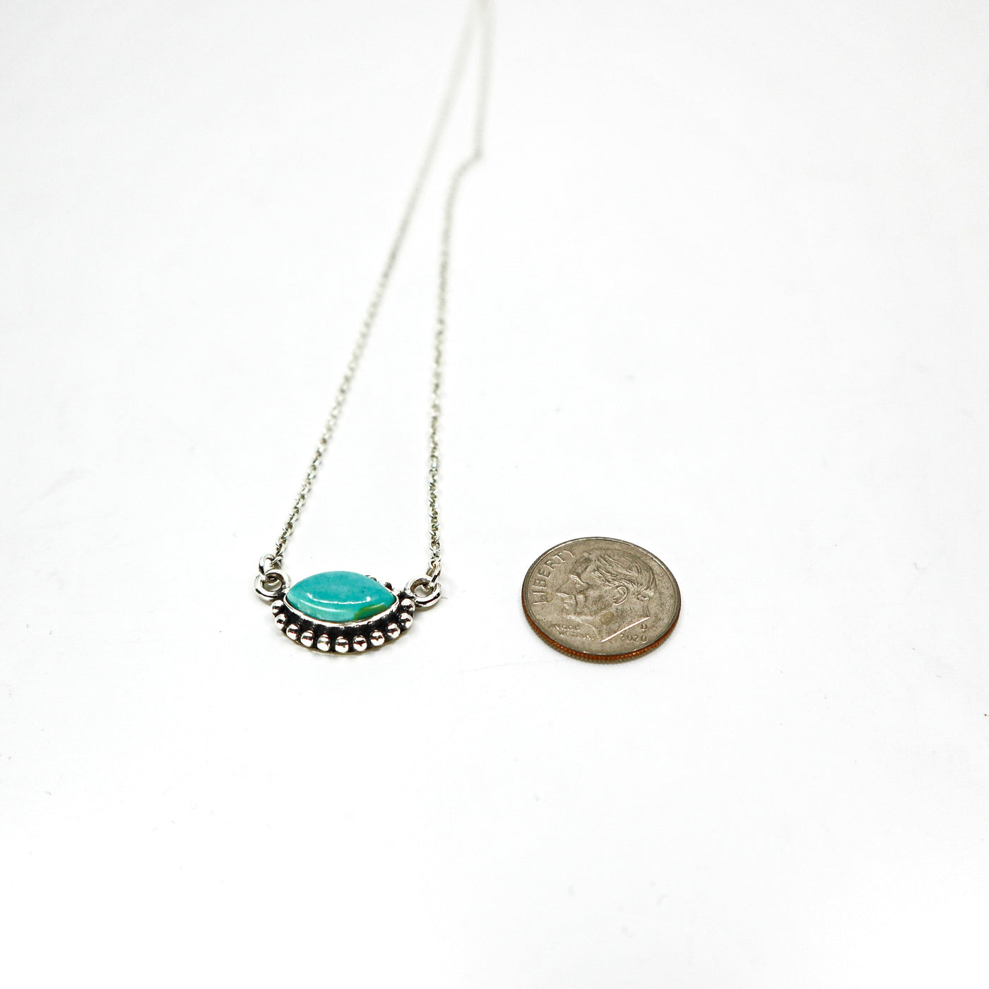 Handmade sterling silver necklace with turquoise oval pendant next to a coin for size comparison