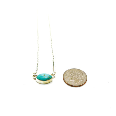 Handmade sterling silver necklace with oval turquoise pendant next to a dime for size comparison