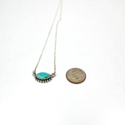 Handmade sterling silver necklace with turquoise oval pendant next to a coin for size comparison