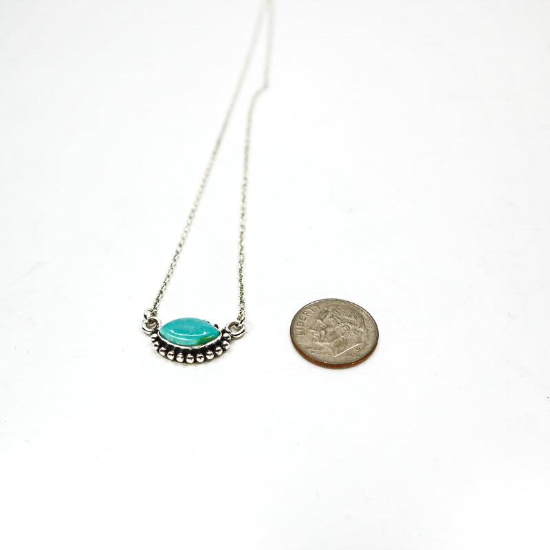Handmade sterling silver necklace with turquoise oval pendant next to a coin for size comparison