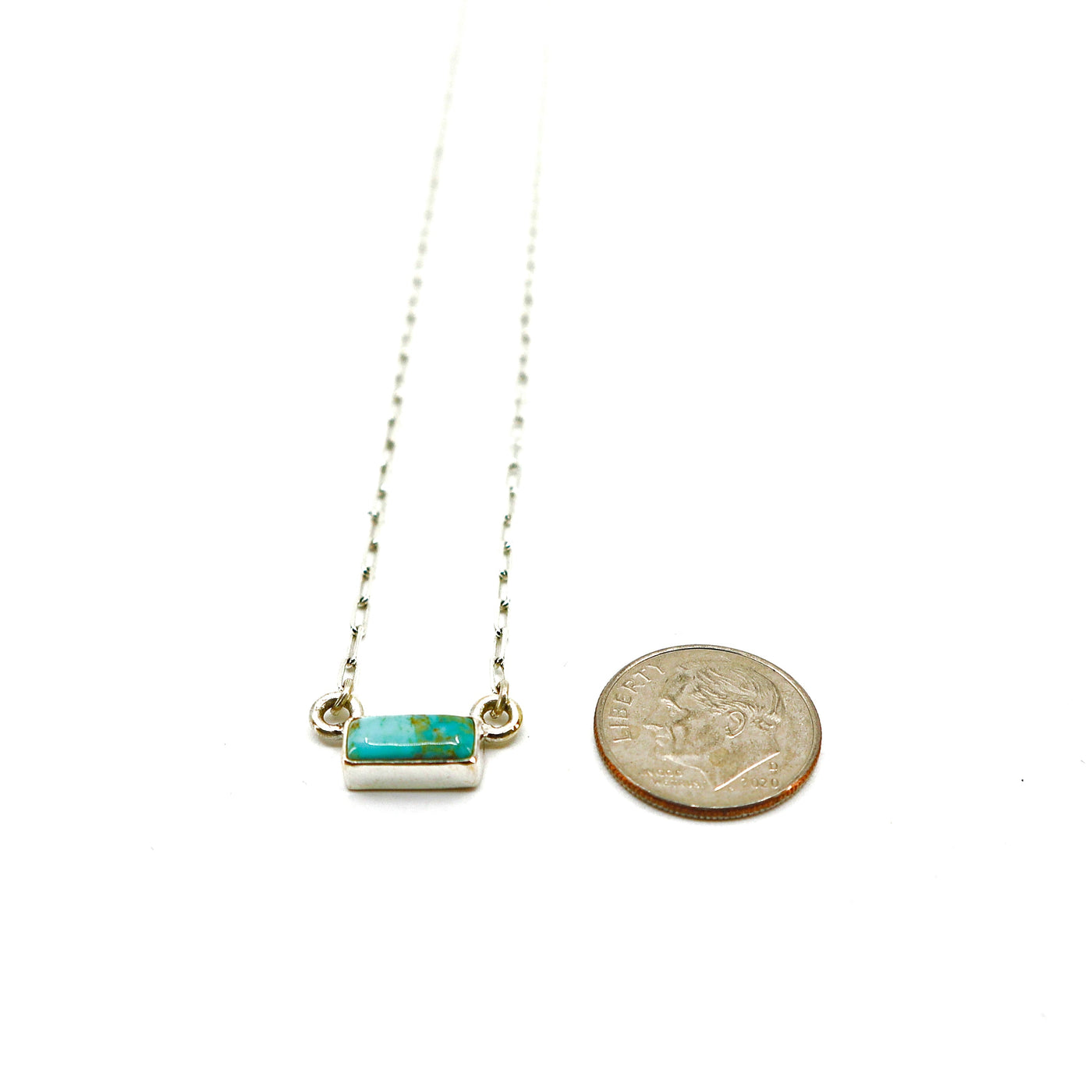 Handmade sterling silver necklace with small turquoise bar pendant next to a US dime for size comparison