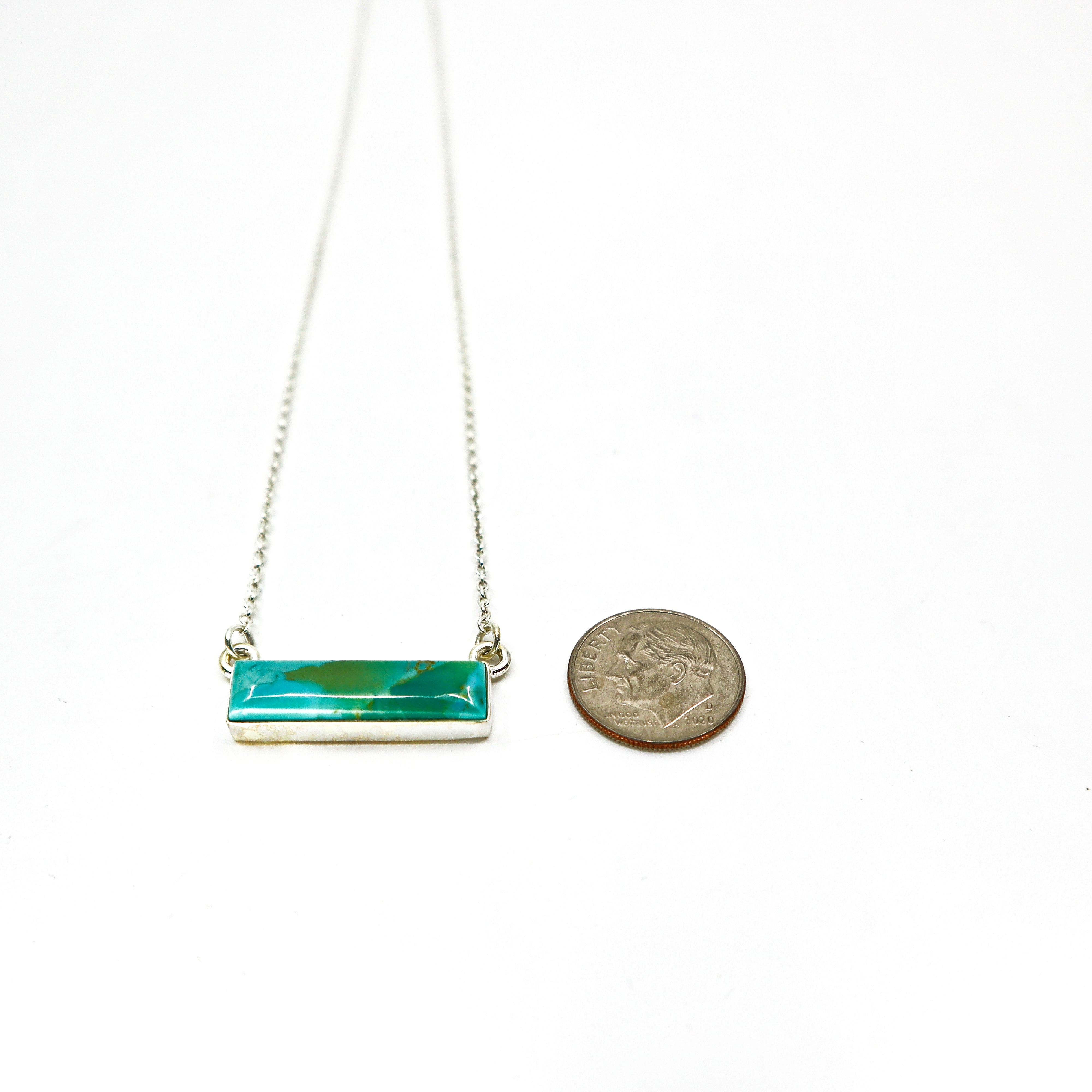 Handmade sterling silver necklace with a large turquoise bar pendant next to a dime for size comparison