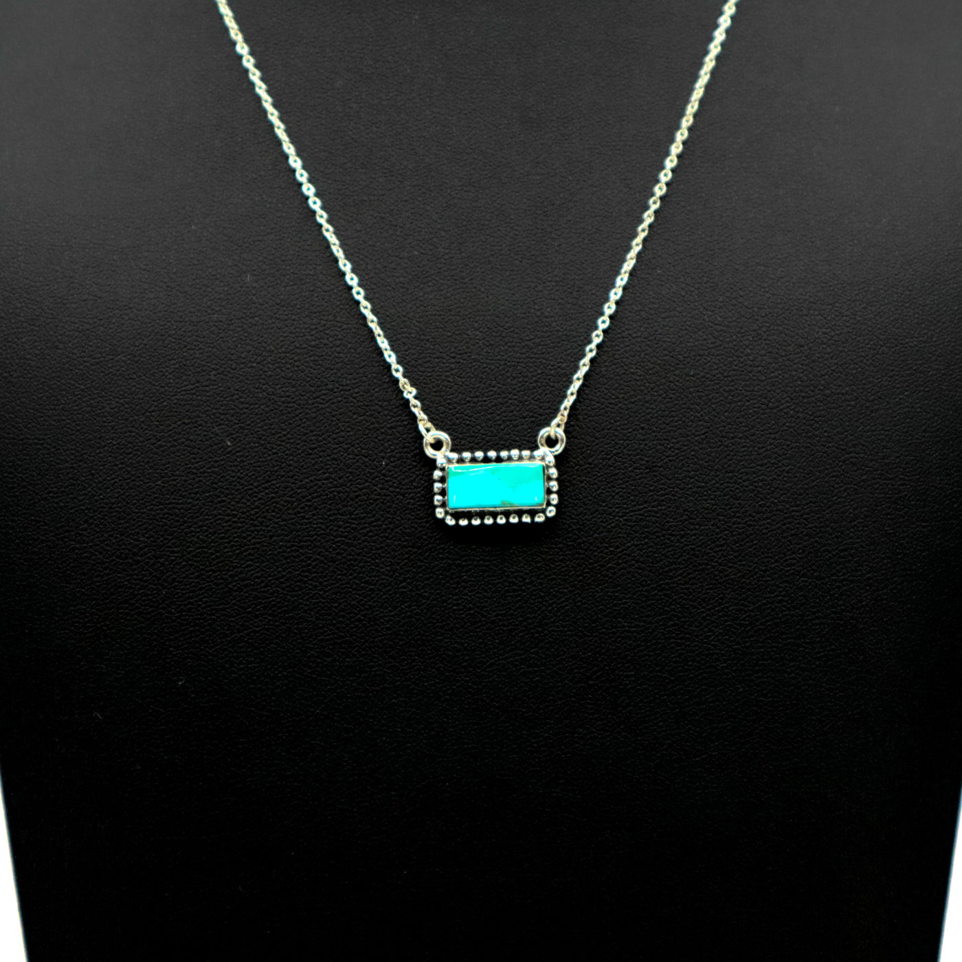 Sterling silver necklace with intricate border and small turquoise bar pendant
