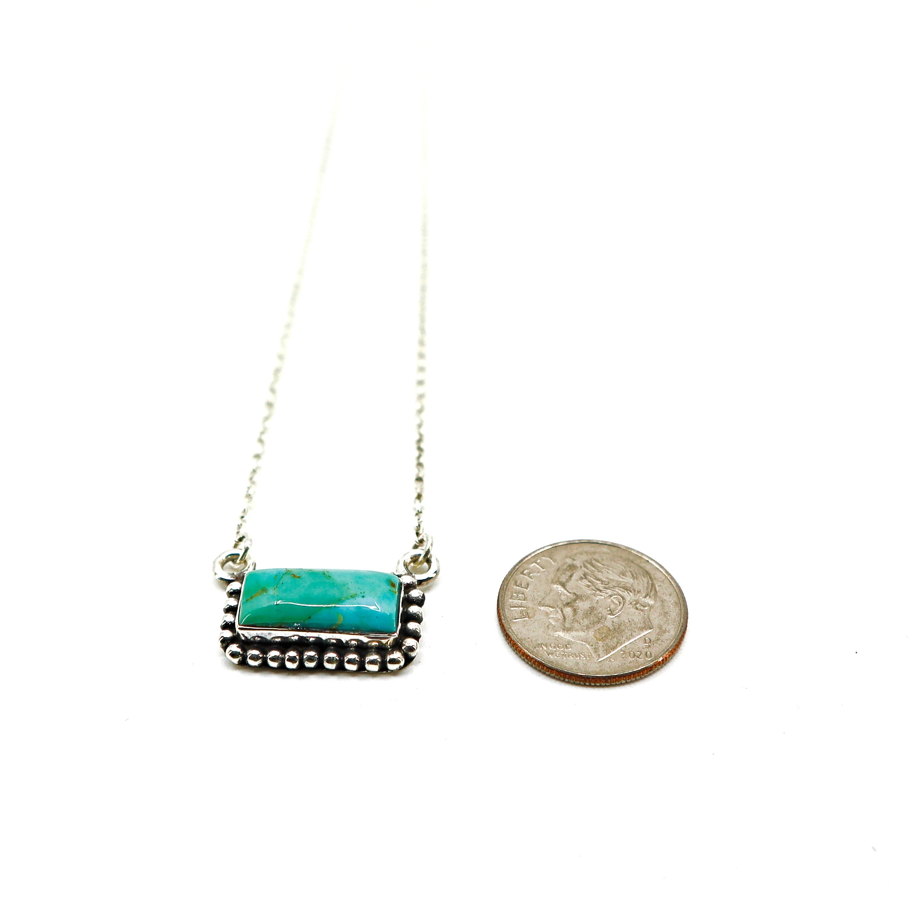 Sterling silver necklace with turquoise stone and intricate border next to a coin for size comparison