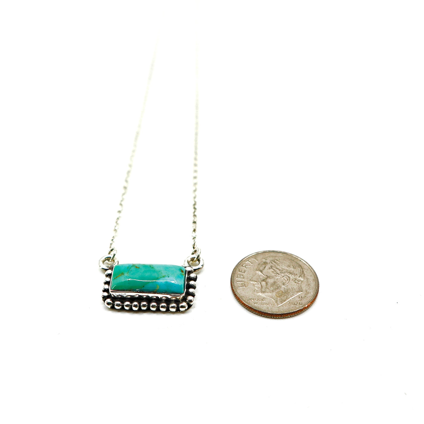 Sterling silver necklace with turquoise stone and intricate border next to a coin for size comparison