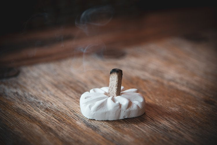 Wood incense brick on holder with gentle smoke rising.