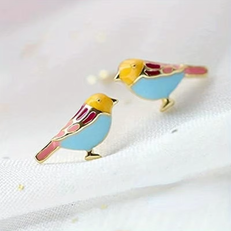 18k gold plated bird enamel stud earrings on fabric backdrop.