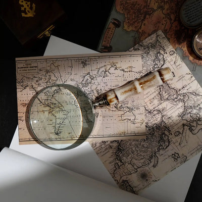 Decorative magnifying glass with smooth resin handle and silver electroplated steel frame on vintage maps.