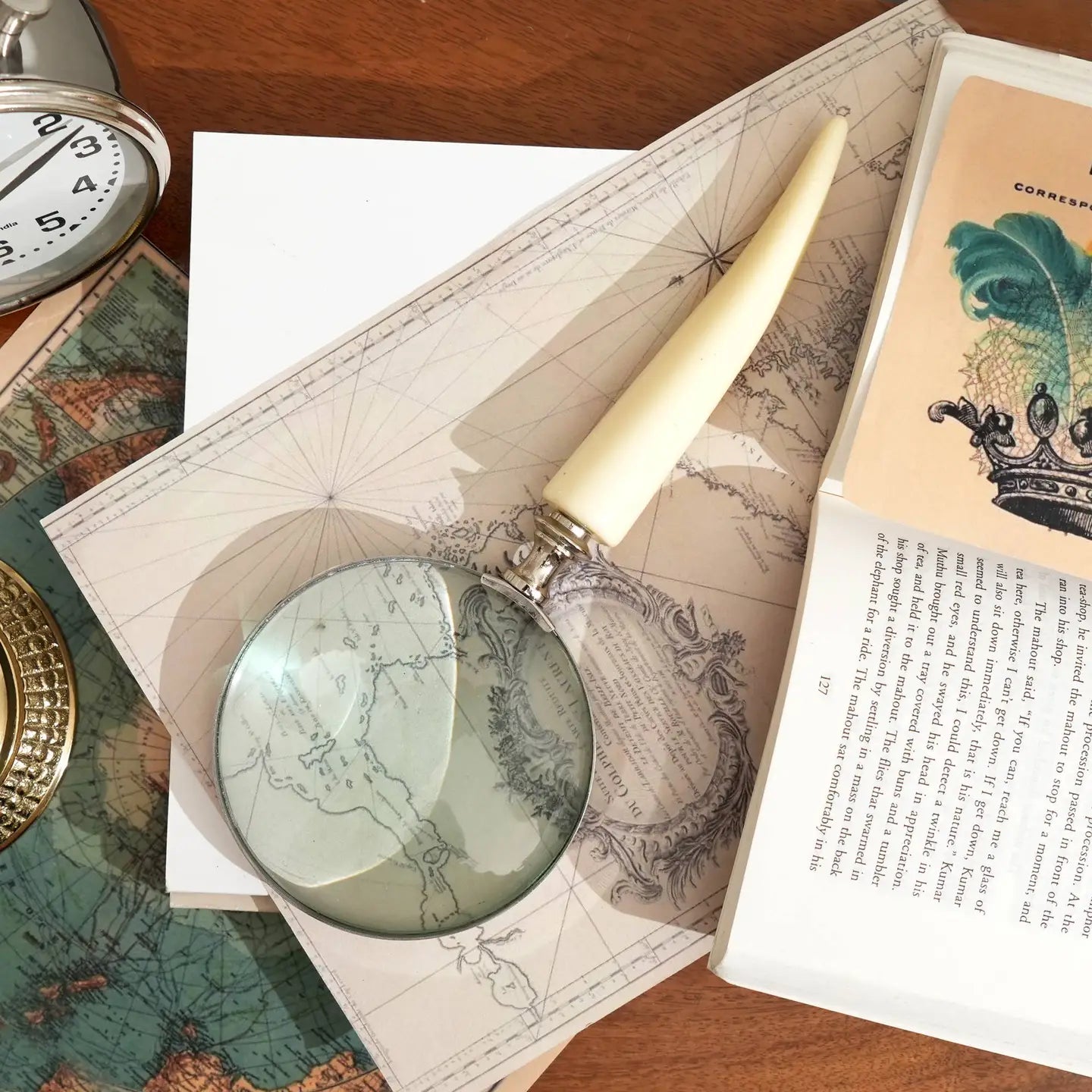 Decorative magnifying glass with ivory resin handle and silver electroplated finish placed on vintage maps and book.