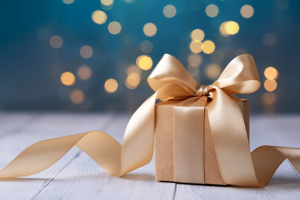 Elegant gold free gift box with ribbon on blue bokeh background
