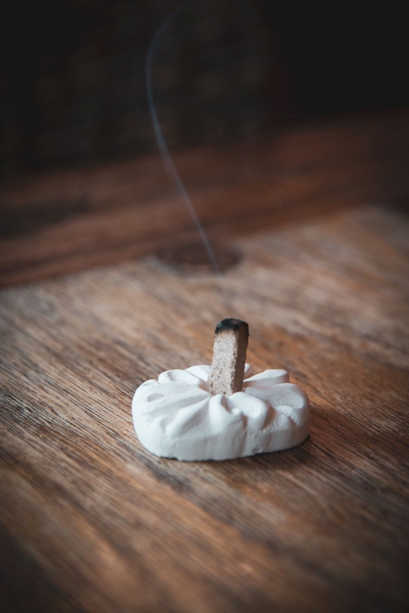 Natural Wood Incense Brick burning on a white holder, releasing aromatic smoke.