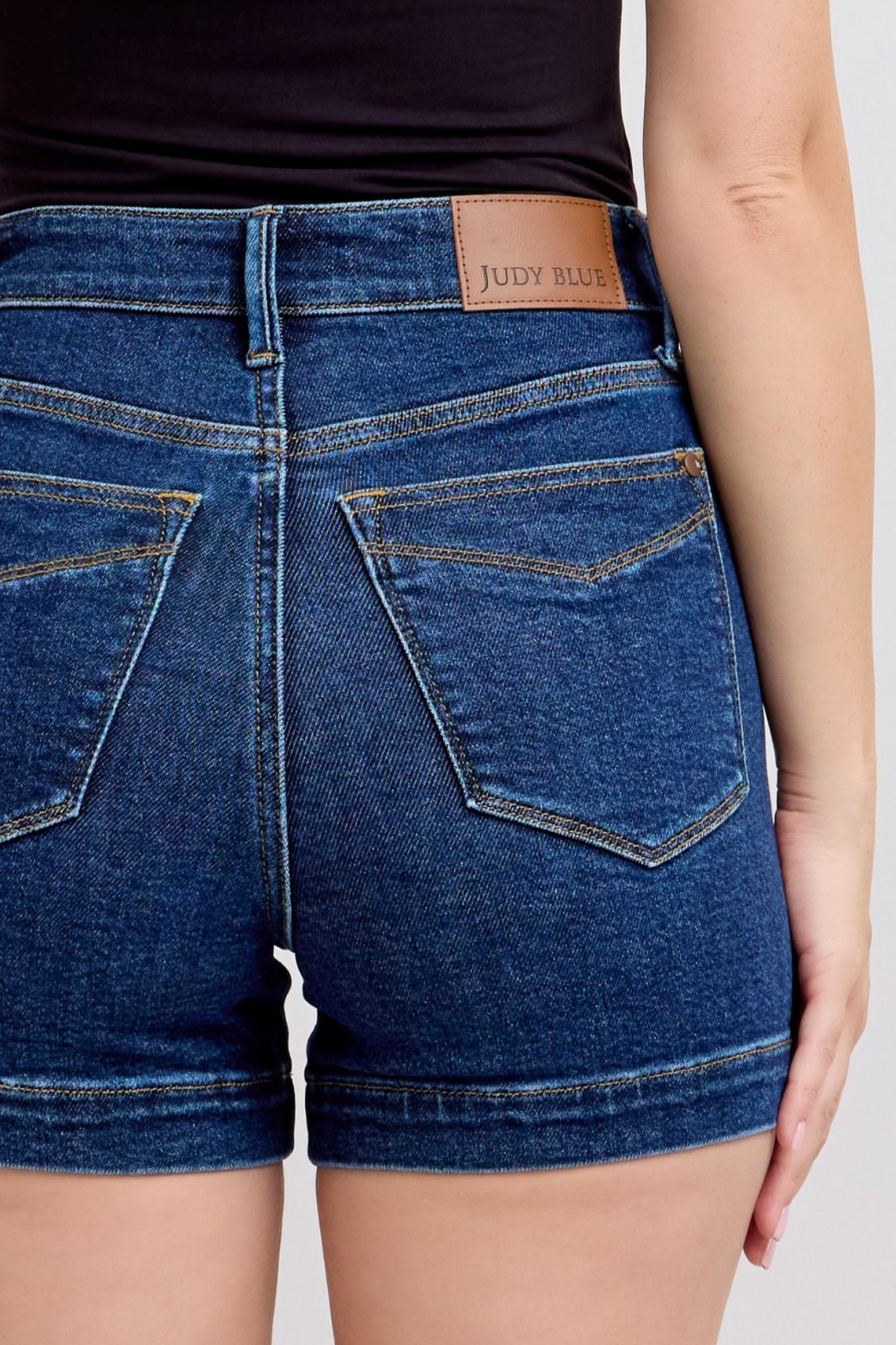 Back view of woman wearing high waist Judy Blue denim shorts with leather brand patch and classic stitching.