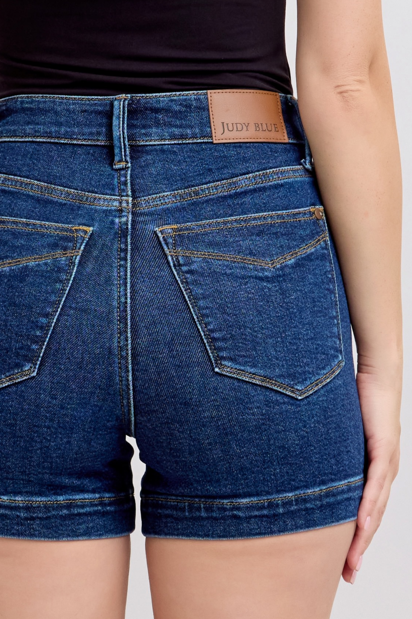 Back view of woman wearing high waist Judy Blue denim shorts with leather brand patch and classic stitching.